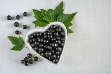 Currant berries in a white heart-shaped bowl on a white wooden surface