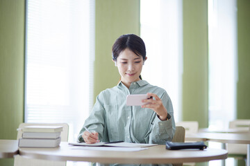 図書館にてスマートフォンを使用して勉強をする日本人の女性