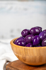 Blueberry fermented olives at wooden bowl. Purple olives on a white wood background. Mediterranean food. vegan food. Close up
