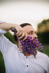 Young man with bouquet of lupines like a beard. Sunset or sunrise, bright evening light