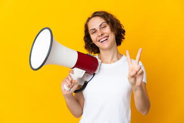Young English woman isolated on yellow background holding a megaphone and smiling and showing...