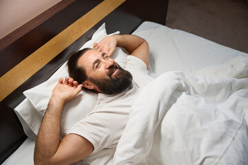 Middle-aged male lies on a snow-white bed