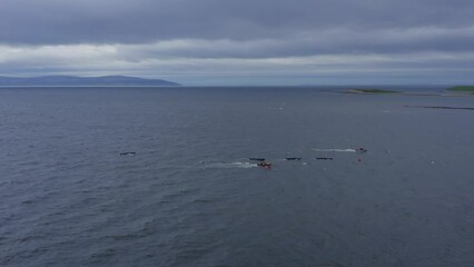 Sideview aerial of currach boat canoes paddling in open ocean with support vessel near by
