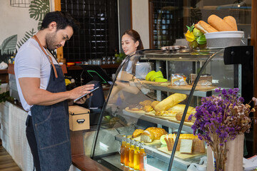Small business couple lifestyle concept, multitask Asian coffee shop owner man or worker checking online bakery order by using technology tablet, barista woman making coffee ordering by modern machine