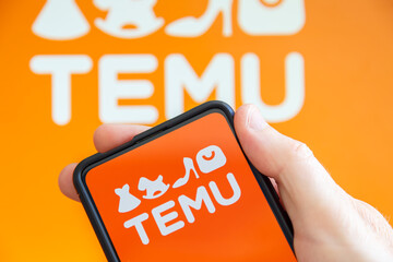 Hand holding a mobile phone with Temu logo online marketplace ecommerce computer screen