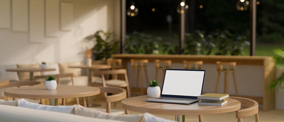A laptop white screen mockup on a wooden round table in a beautiful minimal coffee shop.
