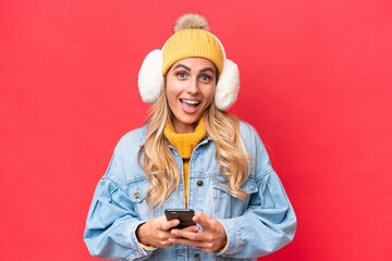 Young pretty Uruguayan woman wearing winter muffs isolated on red background background surprised...