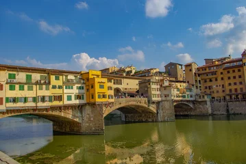 Fototapete Ponte Vecchio Famous medieval bridge Vecchio  through Arno river with jewelry and souvenir shops in Florence, Italy, at sunny day and blue sky