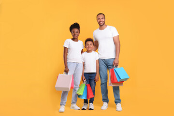Fototapeta premium Family shopping. Happy parents and son with colorful bags on orange background