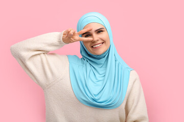 Muslim woman in hijab showing V-sign on pink background