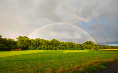 complete rainbow over fields and trees against storm clouds

