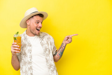 Young caucasian man holding a cocktail isolated on yellow background pointing finger to the side and presenting a product