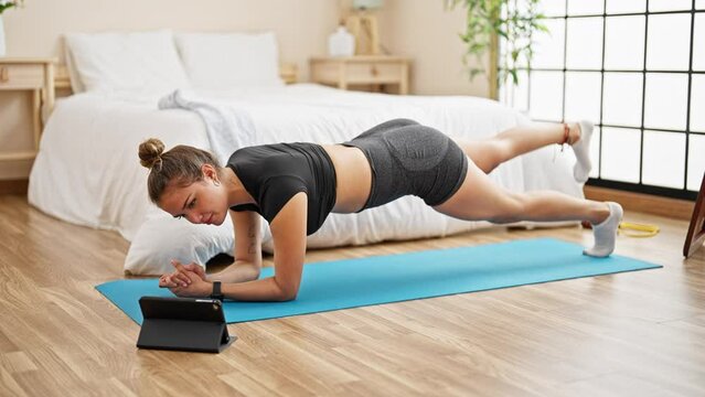 Young beautiful hispanic woman training online abs exercise at bedroom