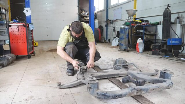 Auto mechanic assembles the subframe of car before installation at garage. Professional bearded repairman with special tool fixing automobile parts at workshop. Concept of maintenance and diagnostic