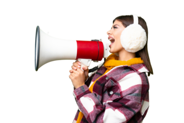 Young Russian woman wearing winter muffs over isolated chroma key background shouting through a megaphone