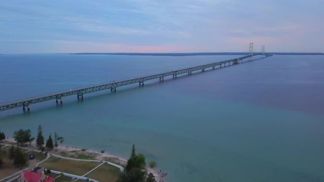 Cinematic aerial drone Mackinaw Bridge lighthouse Michigan sunset dusk purple pink stunning Great Lakes landscape mid summer up north Petoskey Harbor Springs peaceful cars cross bridge forward pan up
