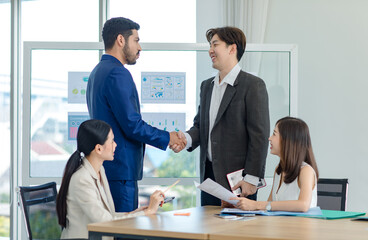 Millennial Asian Indian multinational professional successful businessmen  in formal suit standing shaking hands greeting say hello together in conference meeting room with businesswomen colleagues