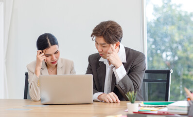 Asian professional successful male businessman explaining discussing brainstorming with female businesswoman colleague in formal business suit via laptop notebook computer in office company workplace