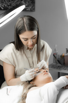 The photo shows eyelash extension process, where the beautician carefully works with each eyelash, giving them a natural look and length. Beauty treatment, relaxation and relaxation in beauty salon