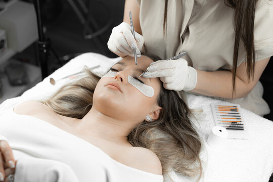 This photo shows the procedure for eyelash extensions with a professional lashmaker in beauty salon. The woman lies relaxed, and beautician applies soft artificial eyelashes, giving her charming look