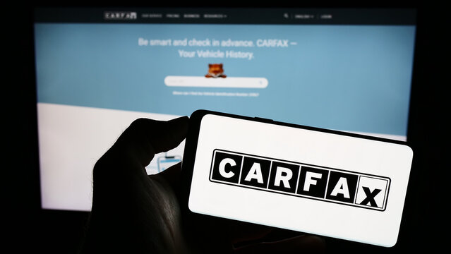 Stuttgart, Germany - 07-29-2023: Person holding cellphone with logo of US vehicle data company CARFAX Inc. on screen in front of business web page. Focus on phone display.