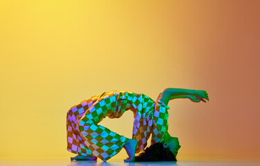 Dynamic image of flexible, artistic young woman dancing against gradient yellow orange background...