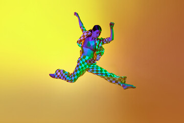 Fototapeta na wymiar Young woman, professional contemporary dancer in motion, in stylish clothes over gradient yellow orange background in neon light. Concept of modern dance style, hobby, art, performance, lifestyle, ad
