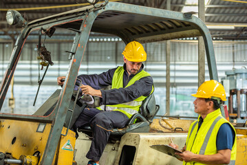 Portrait of forklift truck driver man smiling in old factory warehouse lifting pallet in storage...