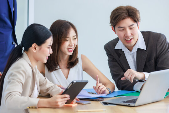 Asian professional successful male businessman explaining discussing brainstorming with two female businesswomen colleagues in formal business suit via laptop notebook computer in office meeting room