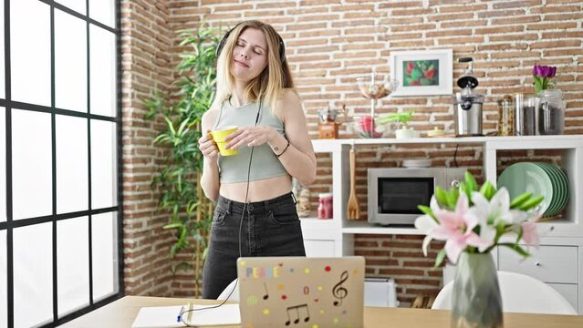Young blonde woman listening to music and dancing drinking coffee at dinning room