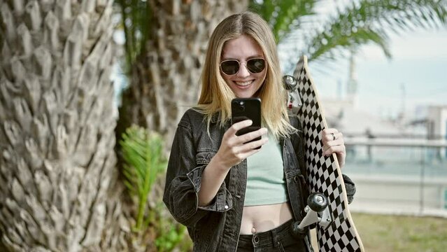 Young blonde woman holding skate make selfie by smartphone smiling at park