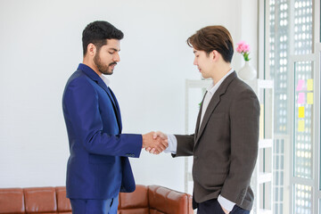 Millennial Asian Indian multinational professional successful businessmen  in formal suit standing shaking hands greeting say hello together in conference meeting room with businesswomen colleagues