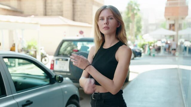 Young blonde woman standing with crossed arms smiling at street