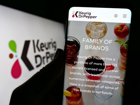 Stuttgart, Germany - 07-30-2023: Person holding cellphone with website of US beverage company Keurig Dr Pepper Inc. on screen in front of logo. Focus on center of phone display.