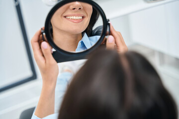 Close up woman dentist patient looking at the mirror at her teeth and smiling