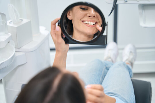 Cheerful woman looking at mirror and enjoying her new dental prosthesis