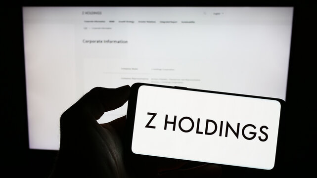 Stuttgart, Germany - 07-30-2023: Person holding mobile phone with logo of Japanese company Z Holdings Corporation on screen in front of business web page. Focus on phone display.