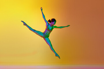 Twine pose. Young talented woman, professional dancer in motion, dancing against gradient yellow orange background in neon light. Concept of modern dance style, hobby, art, performance, lifestyle, ad