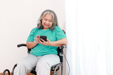 Elderly woman sitting in a wheelchair holding a smartphone watching social media Stay in a room in the house. senior health care