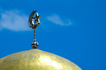 Golden dome mosque and a crescent moon and star symbol with blue sky and light clouds 