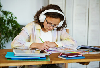Teenage girl drawing colored pens at home with headphones and listen audio or music. Relaxing hobby for teenagers
