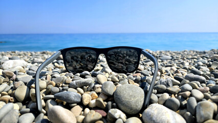 Sunglasses on a pebble beach against the background of the azure sea
