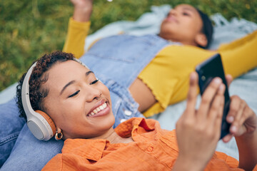 Music, phone and lesbian couple relax at picnic on grass, technology and streaming service app in...