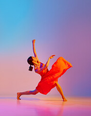 Dynamic image of artistic young woman dancing in elegant red dress against gradient multicolor...