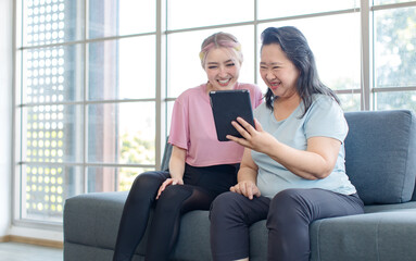 Asian young beautiful daughter and old senior pensioner retirement cheerful happy healthy mother in casual sportswear sitting on sofa couch in living room at home using tablet video call with family