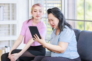 Asian young beautiful daughter and old mother senior pensioner retirement try to see tablet computer sitting on sofa couch in living room at home