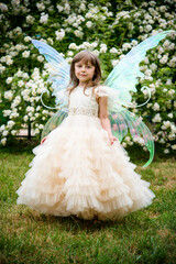 Obraz na płótnie Canvas little beautiful girl in a fairy costume of butterfly with wings in princess dress having fun in roses garden on sunny summer day 