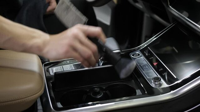 Close up. A woman's hand wipes the lever of the automatic transmission and the buttons of the car console with a brush. Vehicle interior detailing.