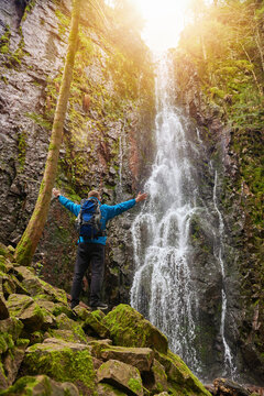 Tourist attraction of Germany - falls of Burgbach Waterfall near Schapbach, Black Forest, Baden-Wurttemberg, Germany. Man hiker in blue jacket standing on stone and looks at flow of falling water