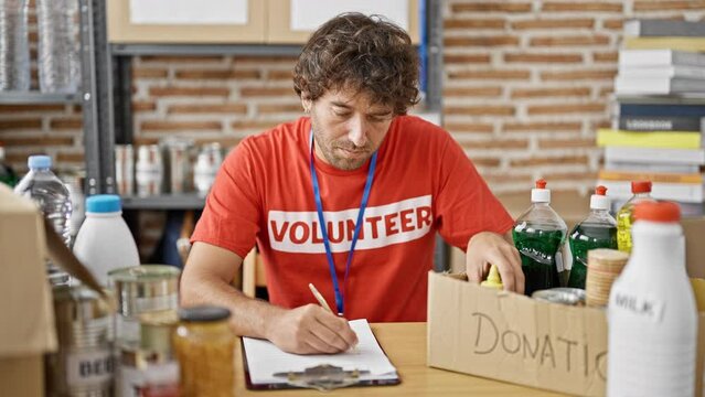 Young hispanic man volunteer writing on clipboard checking products at charity center